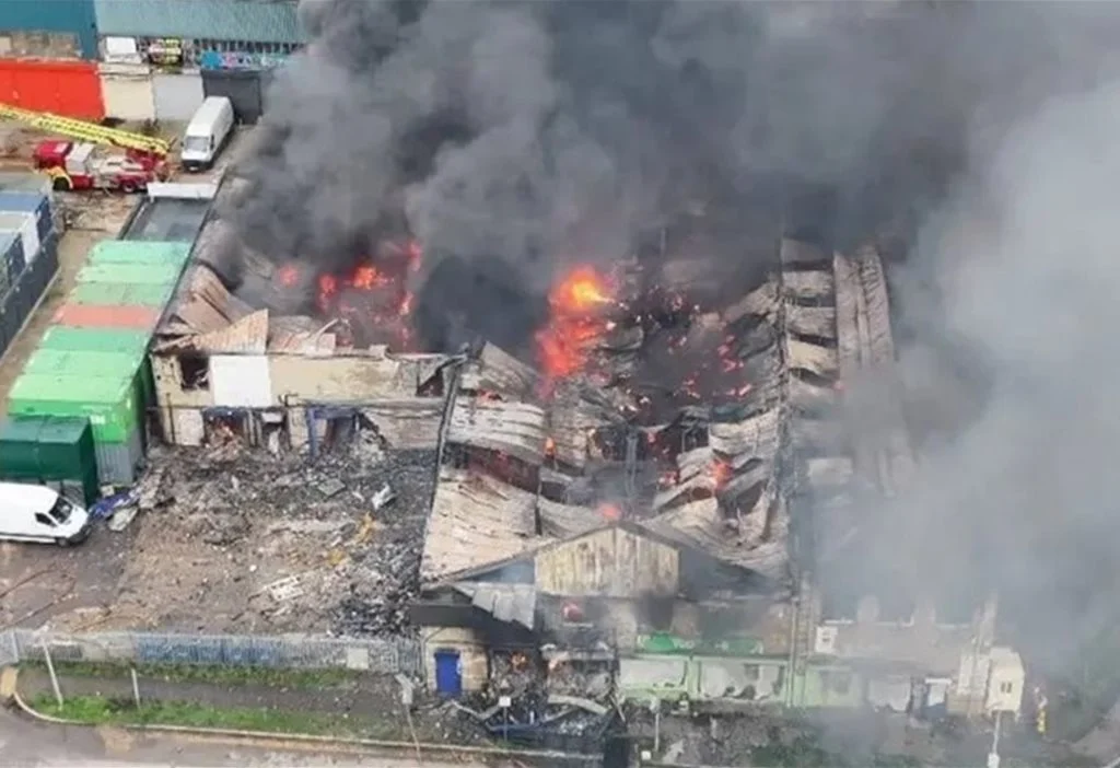 Aerial view of a commercial building ablaze, sending a huge plume of black smoke over the surrounding area